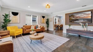 Un vaste salon comprenant un canapé, un fauteuil et une table basse, un coin repas avec des chaises, et une cuisine à l’arrière-plan.