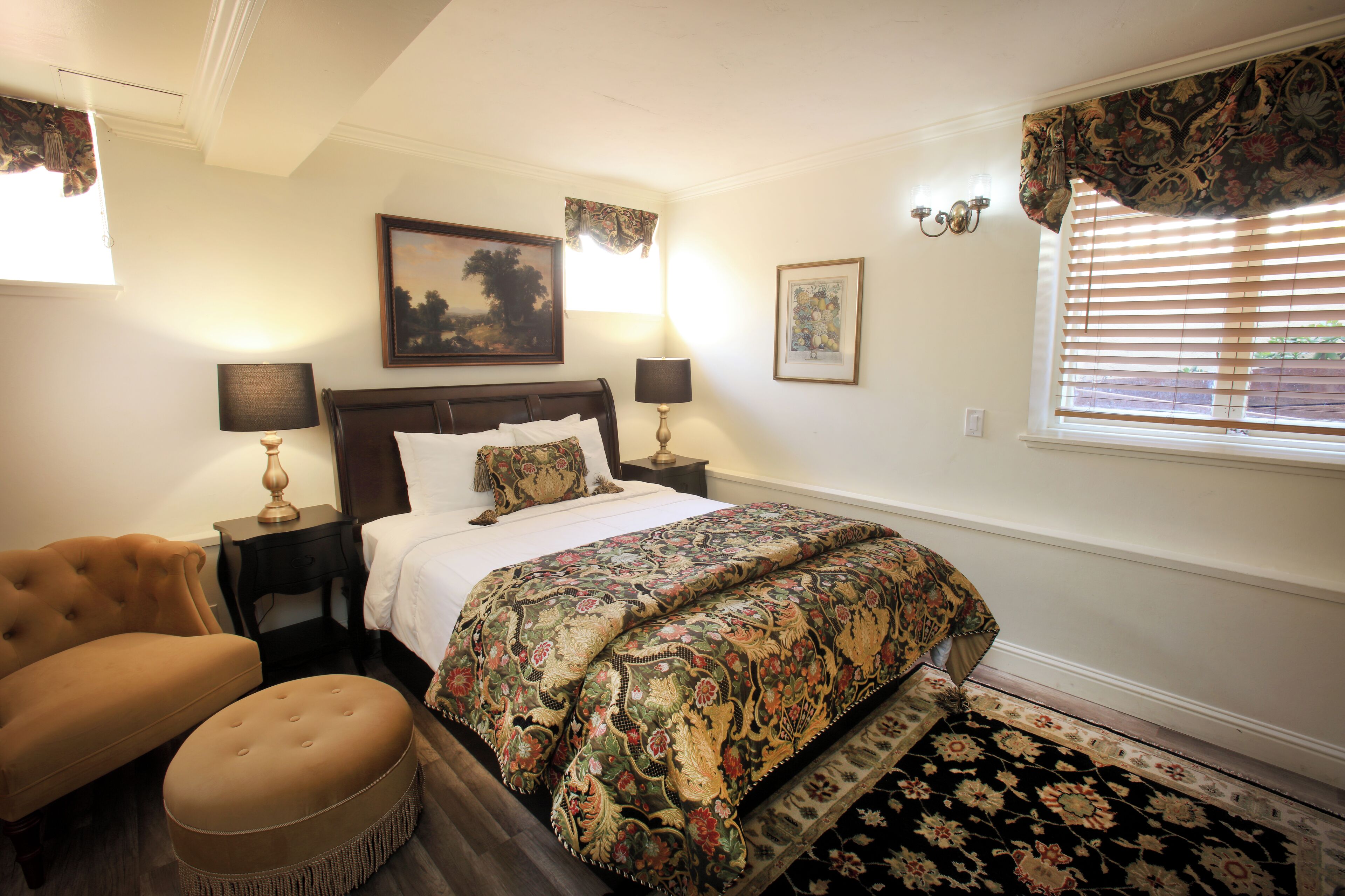 A bedroom with a bed, two bedside tables with lamps, a chair, a rug, and a window with blinds.