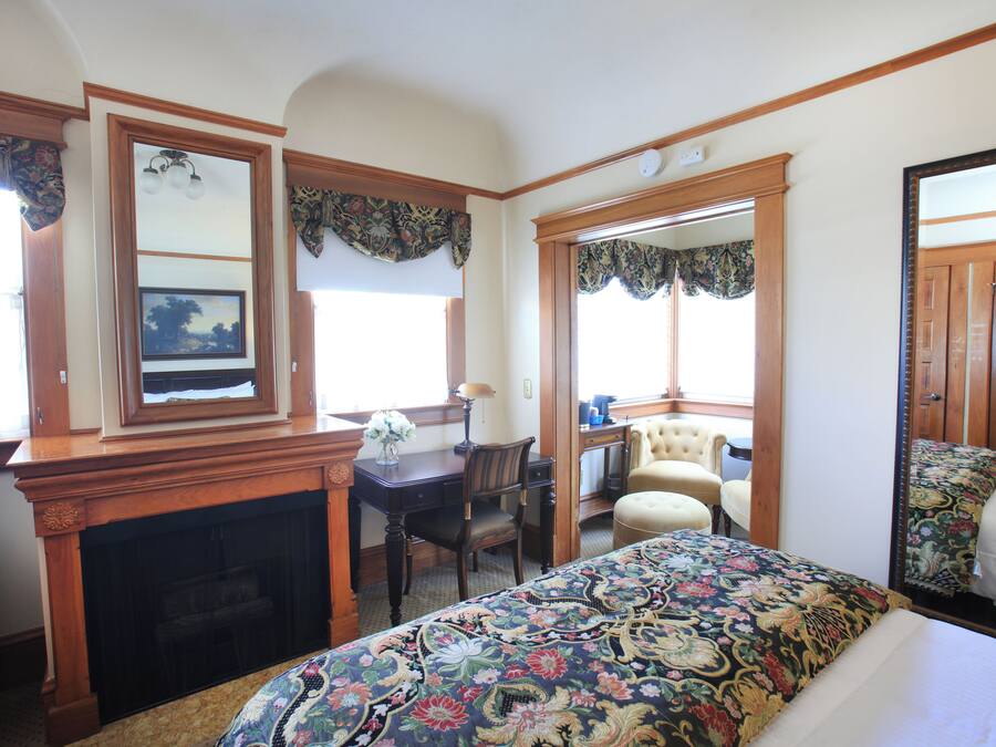 Quarto com cama grande, escrivaninha, cadeira, lareira e espelho.