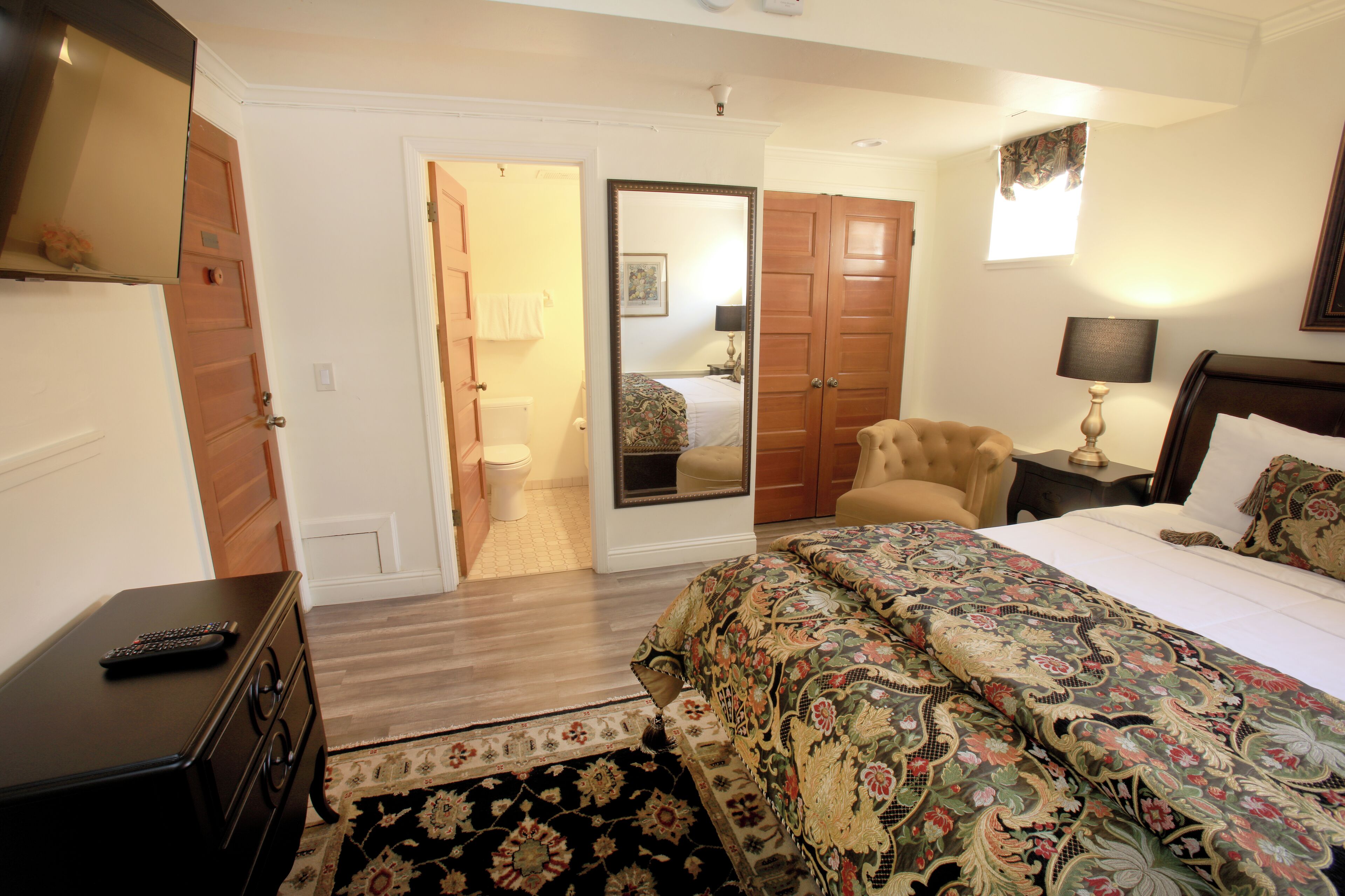 Un dormitorio con cama, una silla, una mesita de noche, un aparador y una puerta que da a otra habitación.