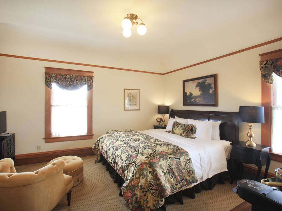 Una habitación de hotel con una cama grande, una silla, un escritorio y un ventanal con cortinas.