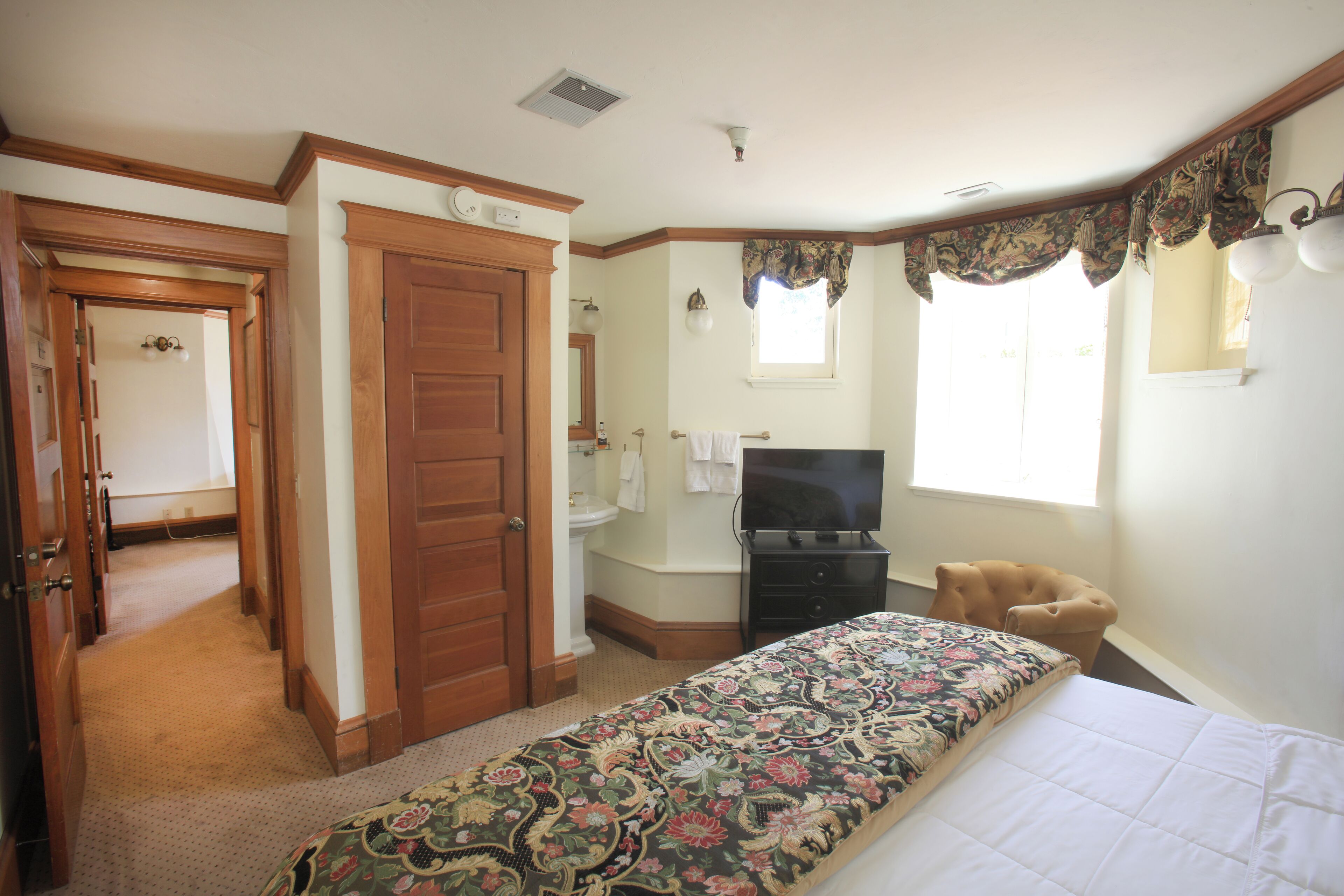 Quarto com cama, televisão, cadeira e janela com cortinas.