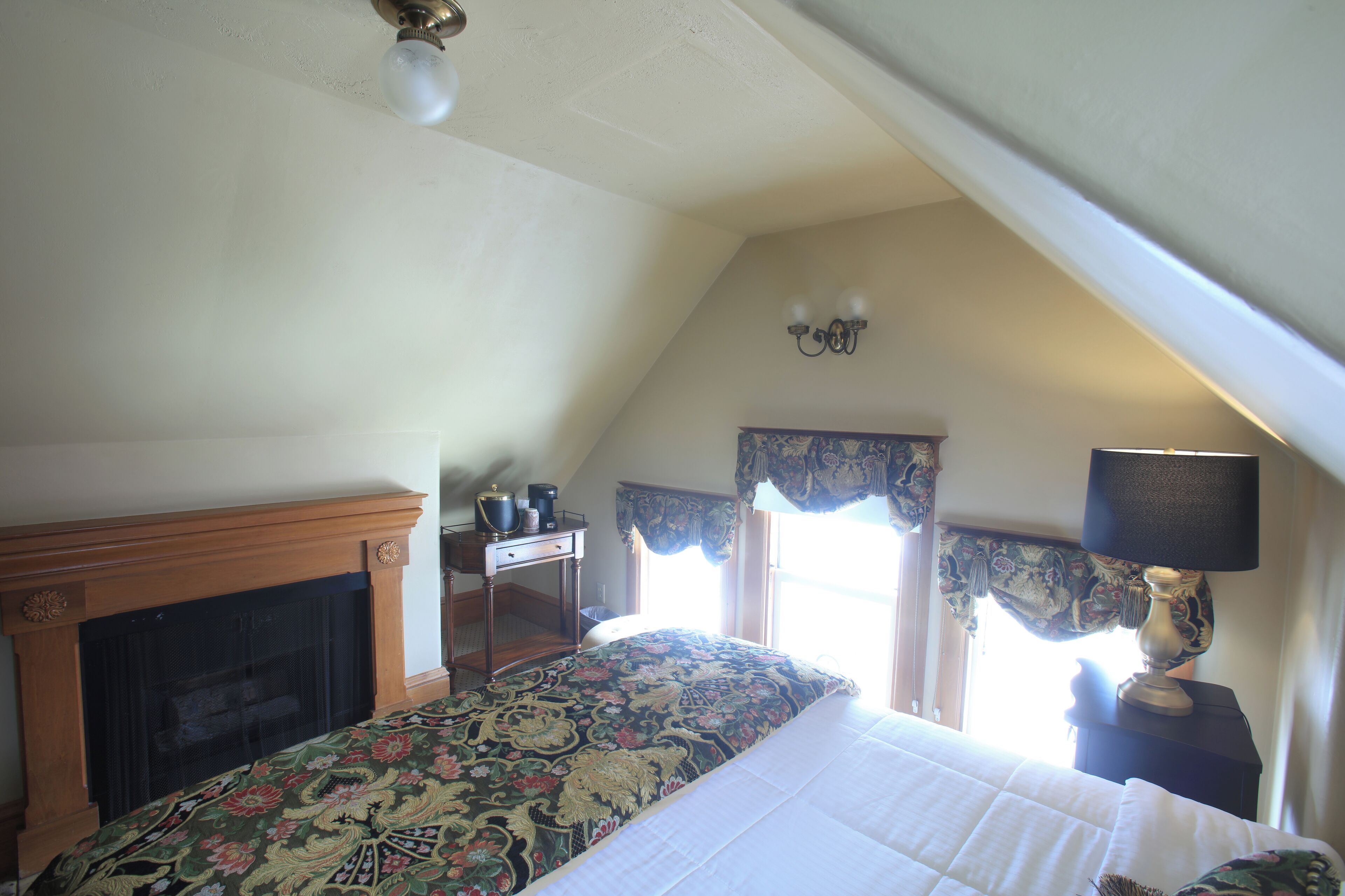 A bedroom with a bed, a fireplace, a desk, and a window with curtains.