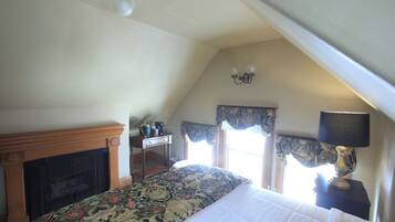 A bedroom with a bed, a fireplace, a desk, and a window with curtains.