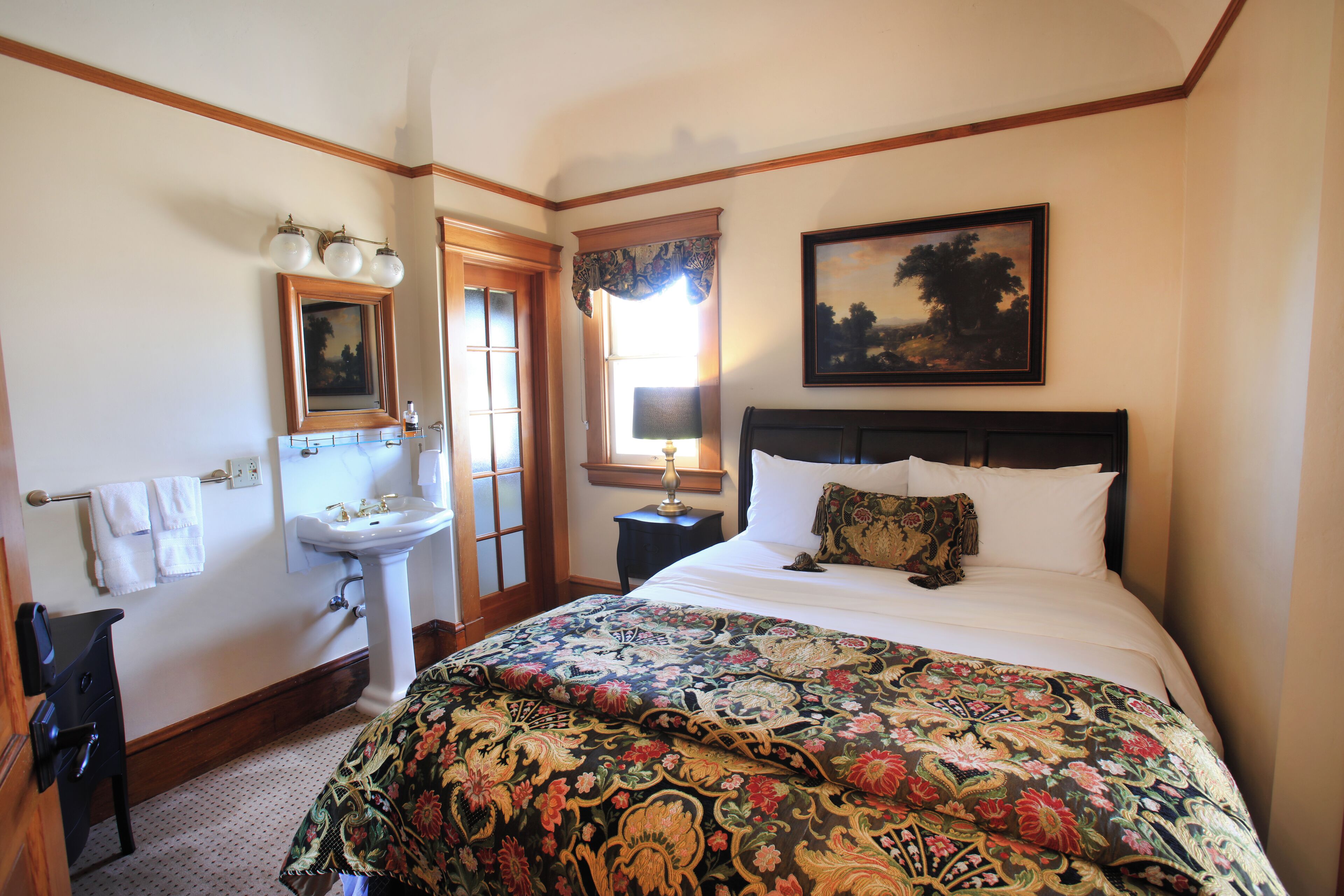 A bedroom with a large bed, a nightstand, a dresser, a mirror, a sink, and a window with curtains.