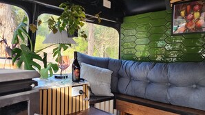 A compact living space with a kitchenette, a sofa, and a dining table. - Unique, Exciting Bus Located on 63 acres with a Cosy woodheater. Luxury. (Mountain River)