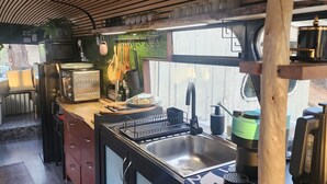 A compact kitchen with a wooden ceiling, a sink, a coffee machine, and various kitchen utensils. - Unique, Exciting Bus Located on 63 acres with a Cosy woodheater. Luxury. (Mountain River)
