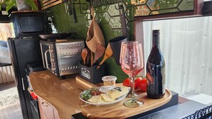 A kitchen area with a wooden countertop, a wine glass, a bottle of wine, and a bowl of cheese and vegetables. - Unique, Exciting Bus Located on 63 acres with a Cosy woodheater. Luxury. (Mountain River)