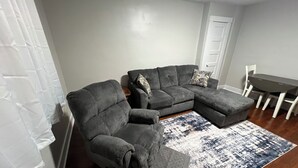 A living room with a grey sectional sofa, a matching ottoman, and a patterned rug.