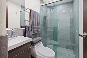 A bathroom with a glass-enclosed shower, a white toilet, a sink with a mirror, and a towel rack.
