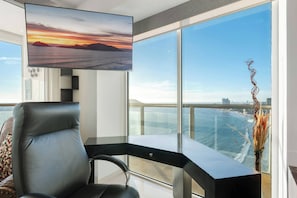 A modern room with a large window overlooking the ocean, a desk, a chair, and a mounted TV.