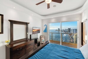Une chambre dotée d’un grand lit, d’une télévision, d’une commode et offrant une vue sur la ville depuis les portes du balcon.