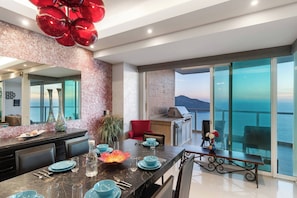 A modern kitchen with a view of the sea, a dining area with blue tableware, and a red chair.