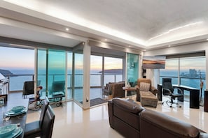 A spacious living area with a view of the sea, a dining table with blue plates, and modern furniture.