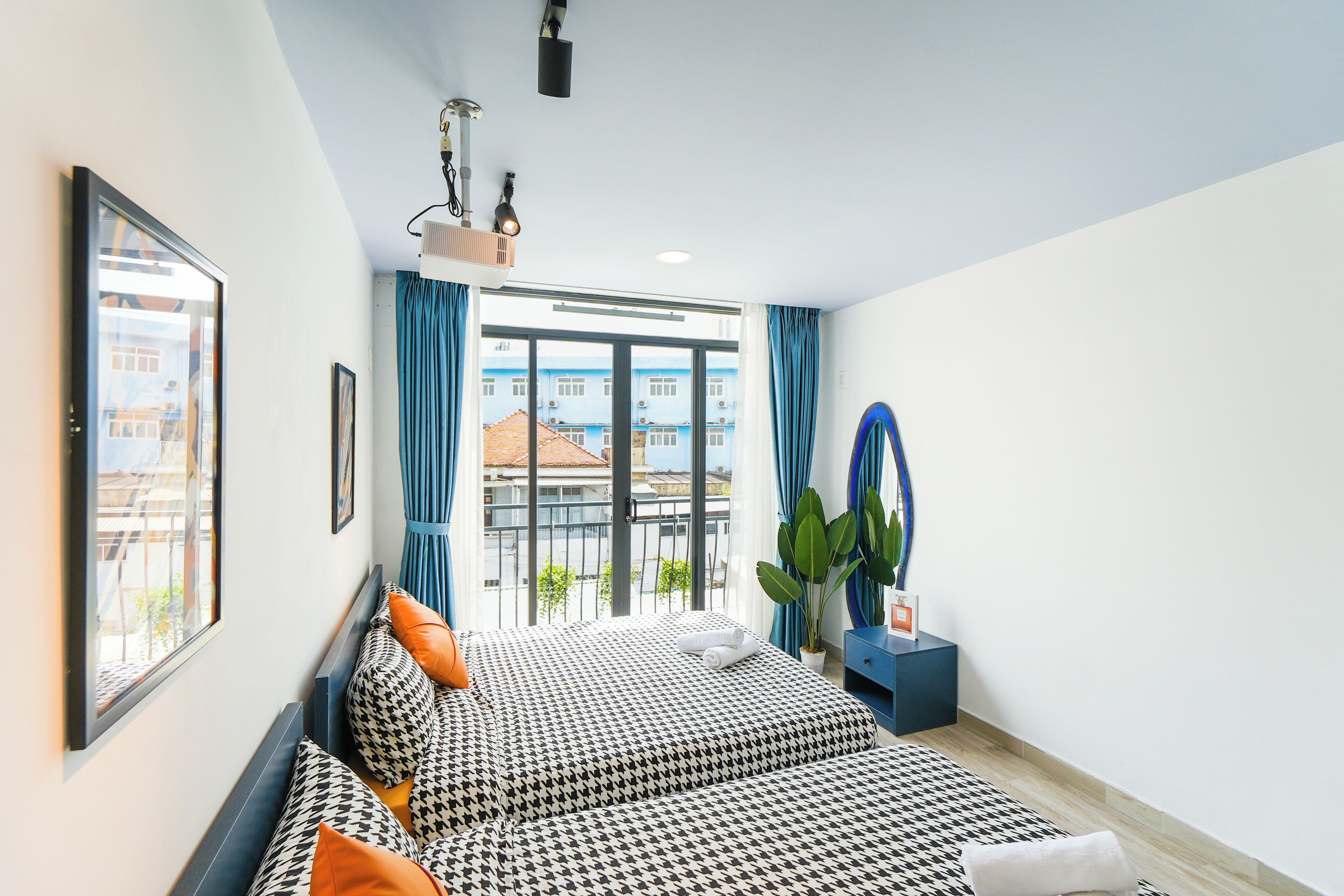 A modern hotel room with a large bed, a seating area, a view of the city, and a small plant.