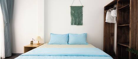 Un dormitorio con cama, armario de madera, mesita de noche, lámpara y un tapiz de macramé en la pared.