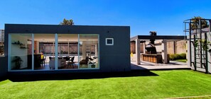 A modern house with a glass-enclosed patio area, a barbecue setup, and a well-maintained lawn.