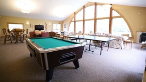 A pool table, a sofa, and a dining table in a room with large windows. - Rivergreen 301, Lincoln (Lincoln)