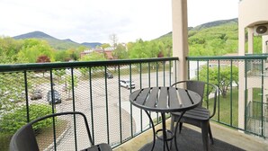 A balcony with a table and chairs, a view of a parking lot, and a building with a red roof. - Rivergreen 301, Lincoln (Lincoln)