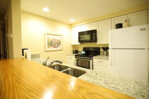 A kitchen with a wooden countertop, stainless steel sink, white cabinets, a black microwave, a white refrigerator, and a framed picture on the wall. - Rivergreen 301, Lincoln (Lincoln)