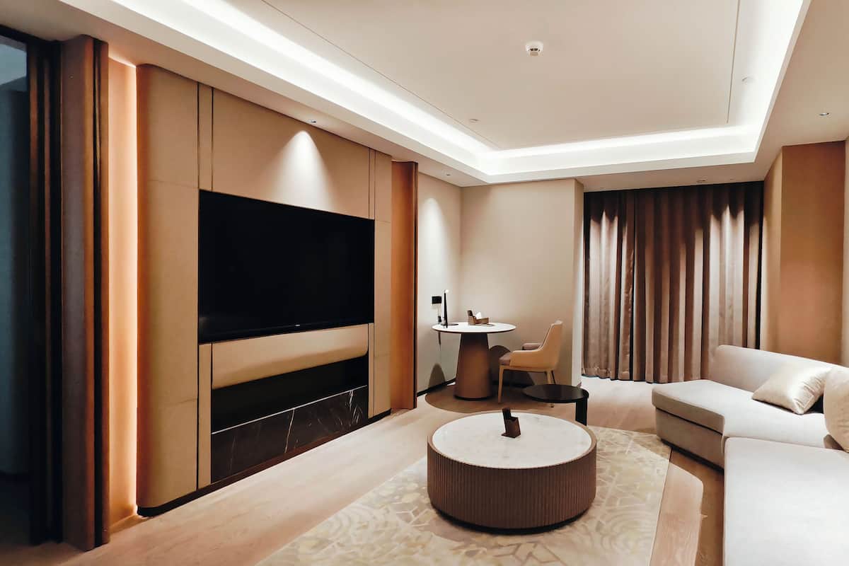 A modern living room with a flat-screen TV, a round coffee table, a sofa, and a dining area with a small table and chair.
