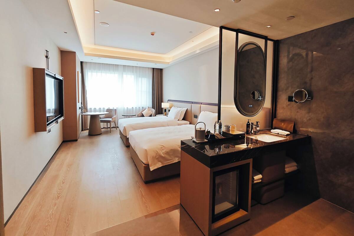 A modern hotel room with a large bed, a desk with a mirror, a small round table, and a TV mounted on the wall.