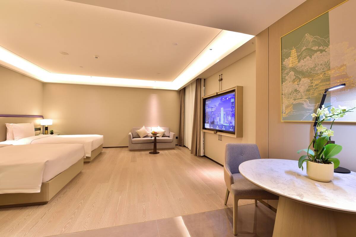 A hotel room with two beds, a sofa, a TV, a dining table, and a potted plant.