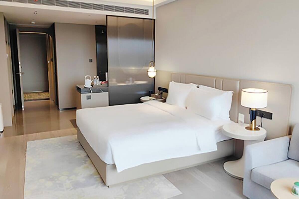 A modern hotel room with a large bed, bedside tables, a nightstand, a sofa, and a bathroom visible through an open door.