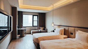 Ein Hotelzimmer mit einem großen Bett, einem kleineren Bett, einem Schreibtisch, einem Stuhl und einem an der Wand befestigten Fernseher.