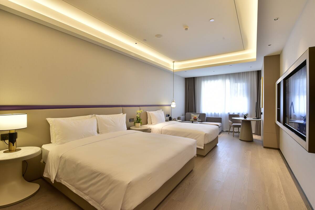 A hotel room with two beds, a desk, a chair, a TV, and a lamp.