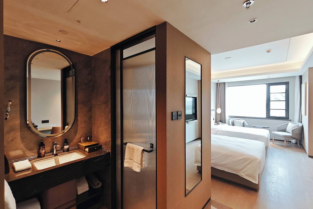 A modern hotel room with a large bed, a separate bathroom with a large mirror, a vanity with a sink, and a television.