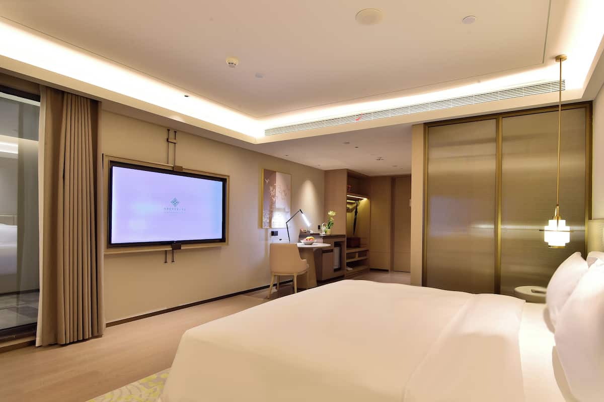 A modern hotel room with a large bed, a desk with a computer, a TV on the wall, and a sliding door closet.
