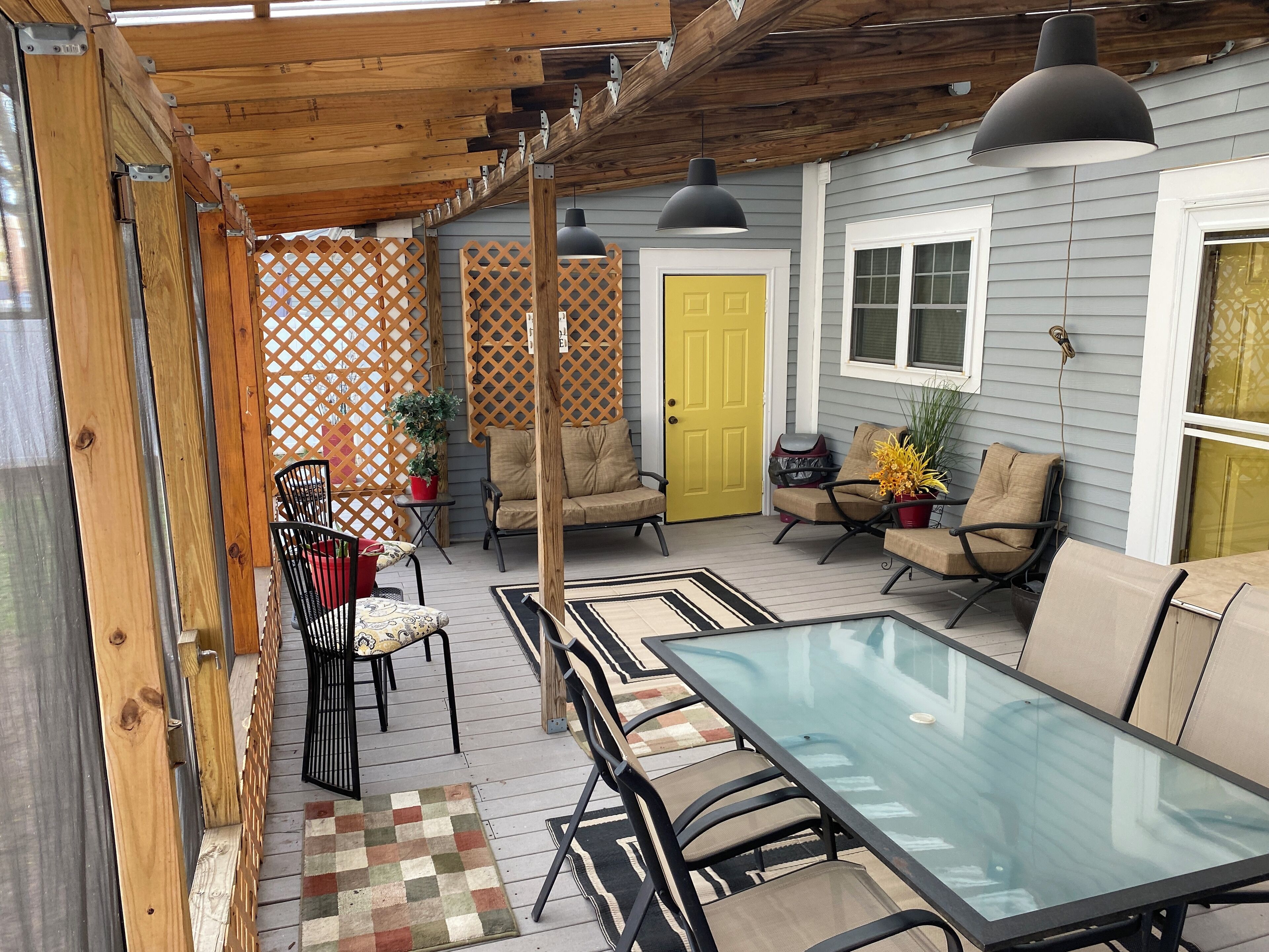 Une terrasse couverte avec une table et des chaises en verre, des poutres en bois et une porte jaune.