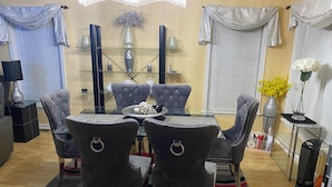 Un comedor con una mesa de vidrio rodeada por cuatro sillas tapizadas, un jarrón decorativo y una mesita auxiliar con una lámpara.