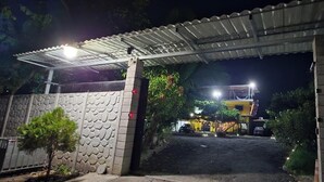 A gated entrance with a covered walkway, a stone wall, and a small tree.
