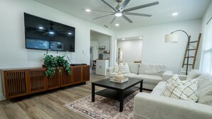 A modern living room with a flat-screen TV, a ceiling fan, a wooden console table with plants, a coffee table, and a sofa.