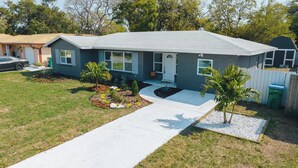 A two-story house with a front porch, a driveway, and a small garden with palm trees.