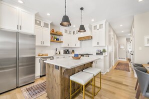 A modern kitchen with white cabinets, a stainless steel refrigerator, a wooden island, and pendant lighting. - Comfort & Charm Near Freeman Park-Downtown- INL (Idaho Falls)