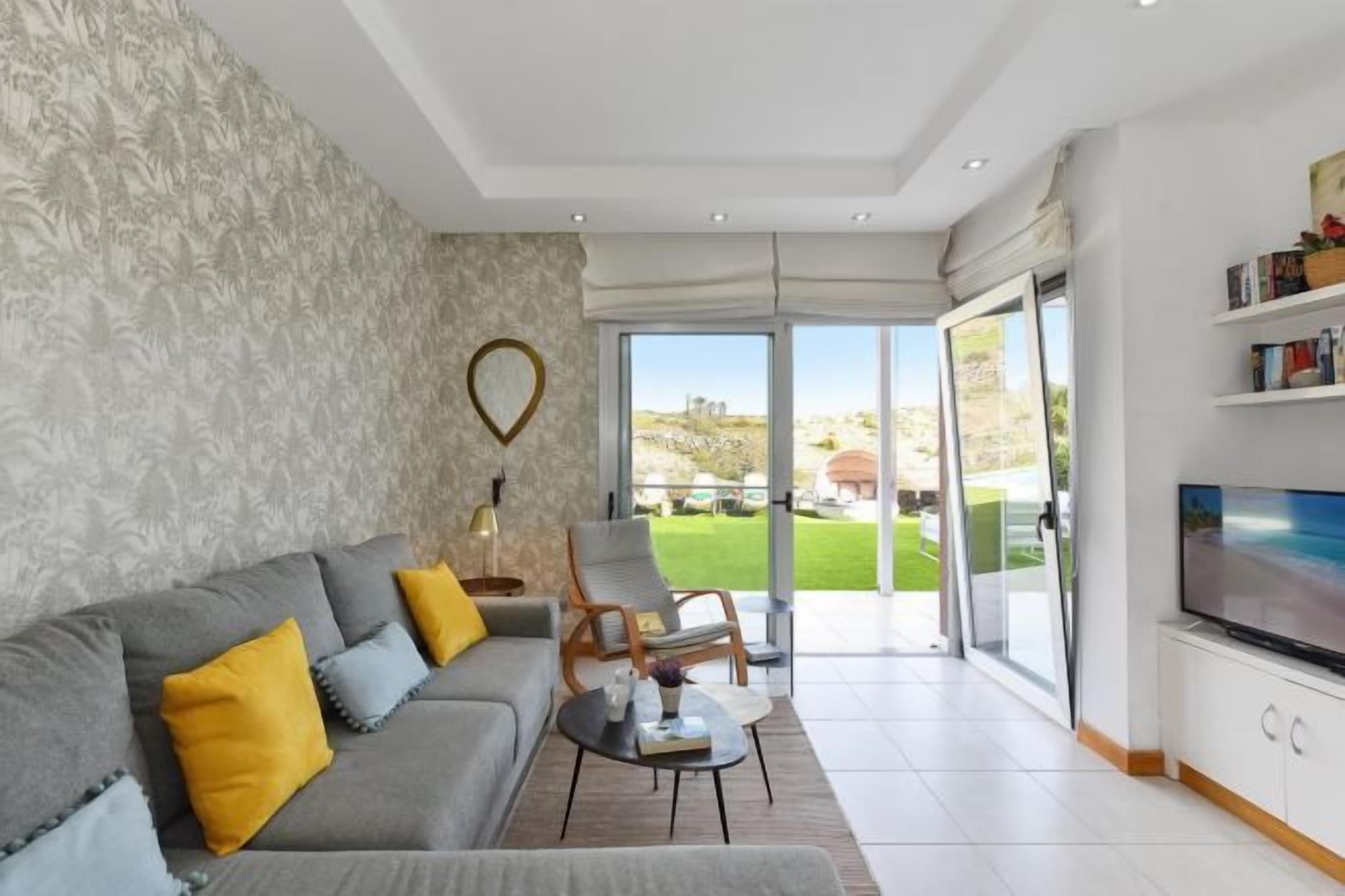 A modern living room with a grey sofa, yellow cushions, a coffee table, and a TV on a white cabinet.