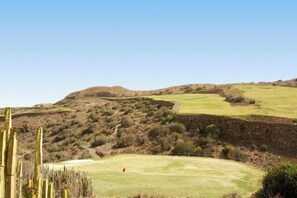 A golf course with a clear sky, cactus plants, and a stone wall. - Vista Golf 30 Salobre by VillaGranCanaria (Comarca Sur)