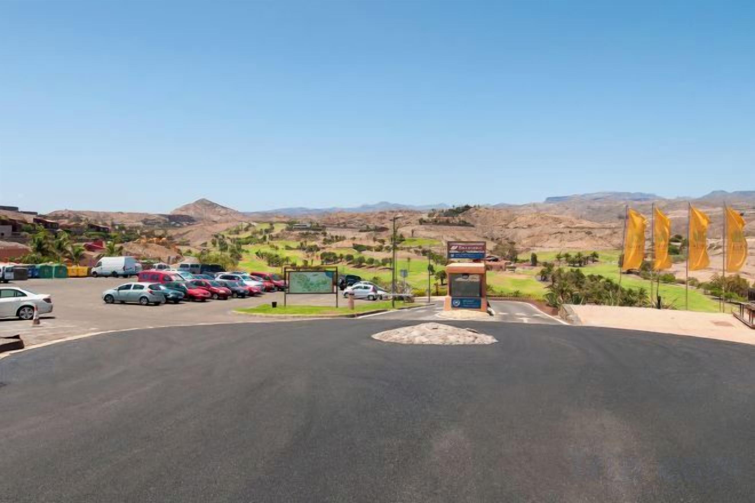 Un estacionamiento con coches, un cartel y vistas de un paisaje montañoso.
