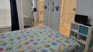 Un dormitorio con cama, televisor, armario y un baño visible a través de una puerta abierta.
