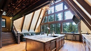 A spacious kitchen with a large island, wooden beams, and large windows offering views of the outdoors. - Lake Views At Rockford Bay - The CDA-frame (Coeur d`Alene)