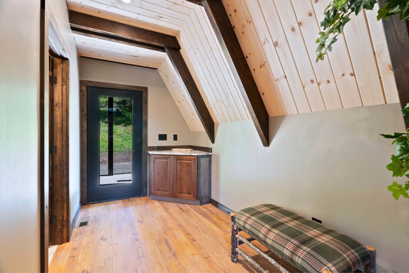 Una habitación con techo inclinado, suelo de madera, un banco y una puerta que da al exterior.