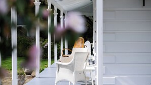 Een overdekt terras met witte rieten meubels en een witte hek.