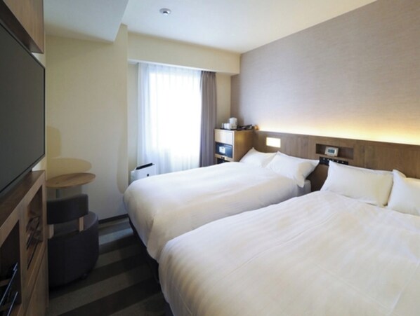 Two single beds with white linens, flat-screen TV, and a small table with chair.