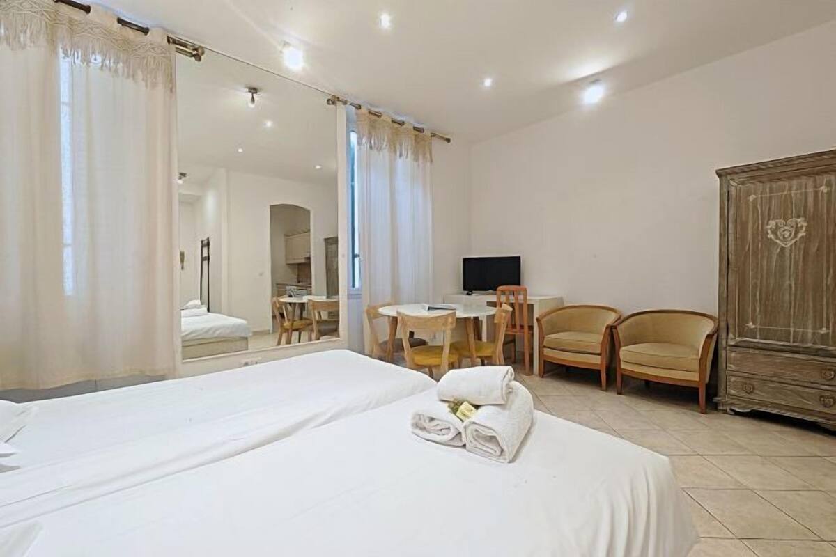 A hotel room with two beds, a desk, two chairs, a TV, and a wardrobe.