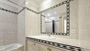 A bathroom with a bathtub, a sink, and a mirror with a decorative border. - Viva Riviera 11 Rue Commandant Andre (Cannes)