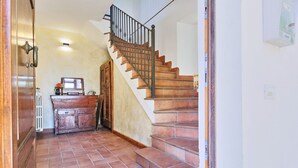 A hallway with a wooden staircase, a radiator, and a wooden cabinet with a mirror and vase.