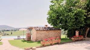A stone building with a tiled roof, a pool, and a view of the countryside.